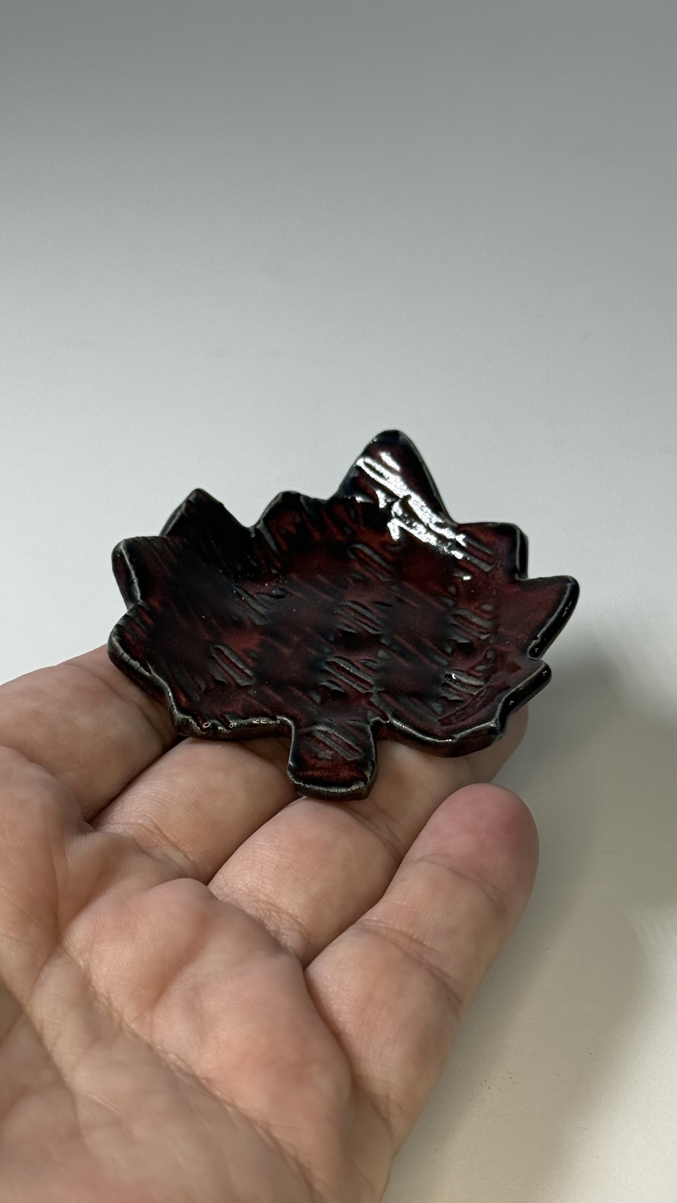 Hand holding a small handmade dark red ceramic leaf dish.