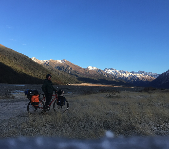 Cycliste dans une vallée avec montagnes enneigées en arrière-plan.