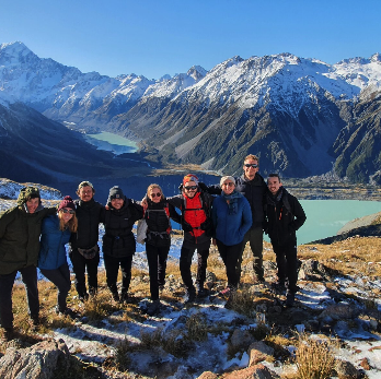 Groupe de sept personnes en randonnée dans un paysage de montagnes enneigées et un lac turquoise en arrière-plan.
