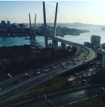 Vue aérienne d'un pont suspendu sur une rivière avec plusieurs voies de circulation et une ville en arrière-plan.