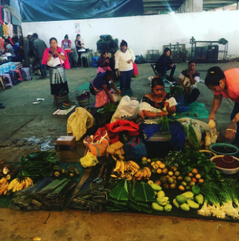 Vendeur(s) et clients dans un marché de fruits et légumes avec des bananes, citron, et autres produits frais