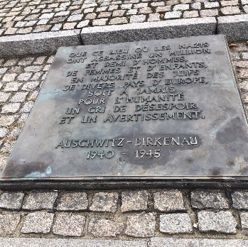 Plaque commémorative en métal avec inscription en français, située sur un pavé. Elle honore la mémoire des victimes de l'Holocauste à Auschwitz-Birkenau, datée de 1940 à 1945.