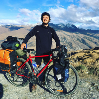 Un homme avec un vélo de route entouré de sacs de voyage, en montagne, à l'extérieur.