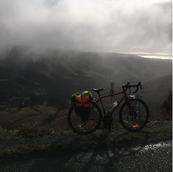 Vélo de route avec sacoches sur un paysage de montagne sous un ciel nuageux.