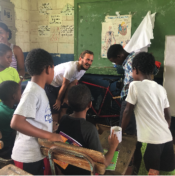 Un groupe d'enfants et un adulte dans une salle de classe, discutant autour d'un vélo, avec un tableau vert en arrière-plan.