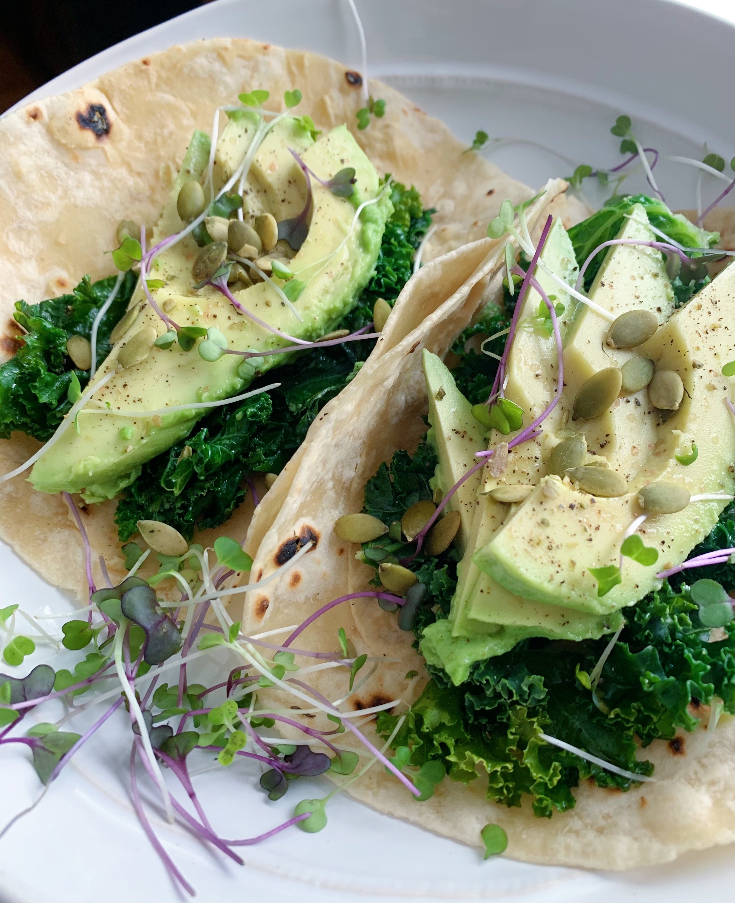 Tacos with avocado, kale, microgreens, and pumpkin seeds on a plate.