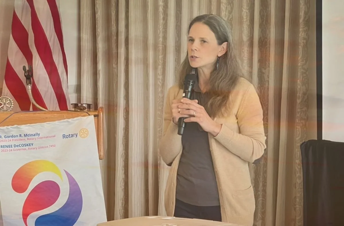 Jill speaks about end of life care planning at a Rotary Club event, with an American flag and a Rotary banner in the background.