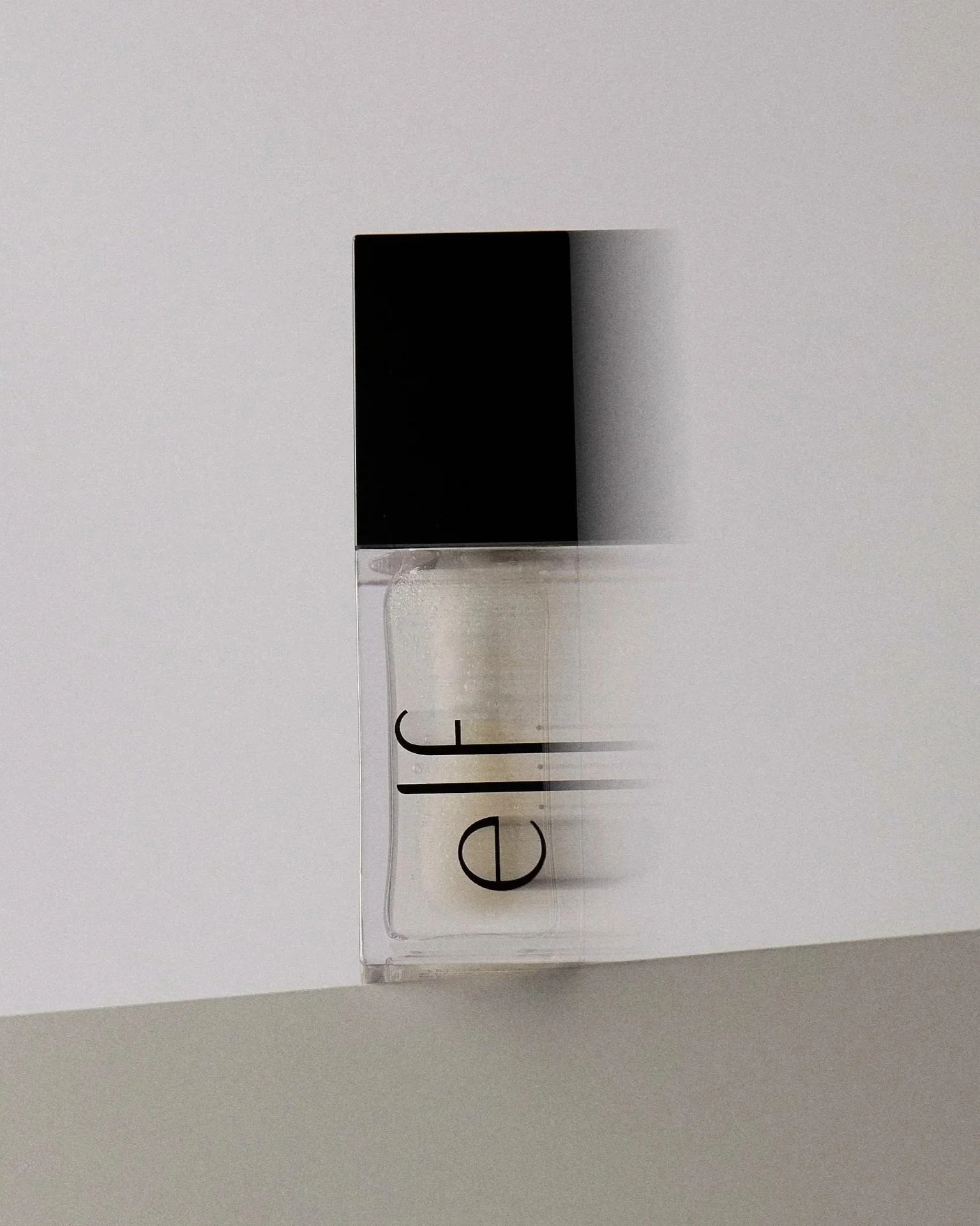 A bottle of clear nail polish with a black cap, placed on a white surface with a light gray background.
