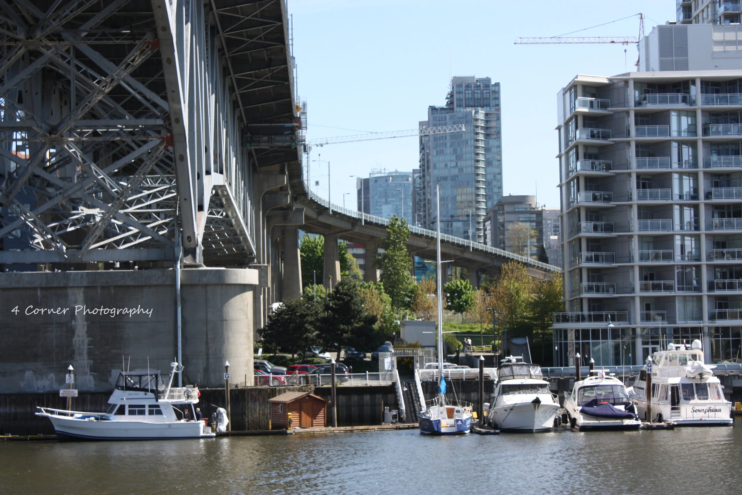 Boats docked along a waterway with high-rise buildings and a bridge in the background.