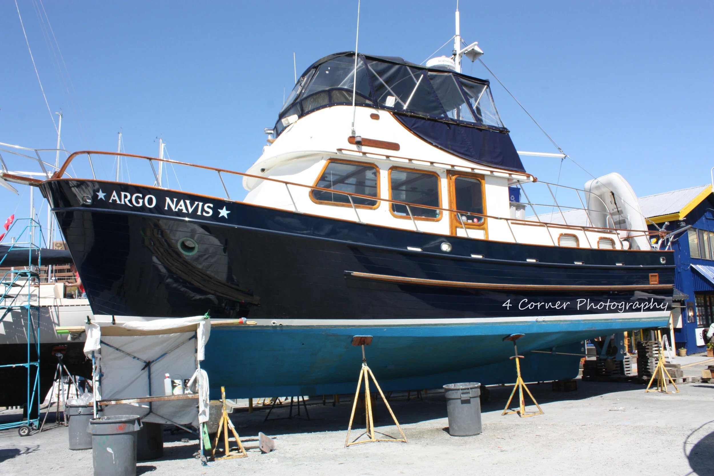 A large boat named Argo Navis on dry dock with a blue hull, white superstructure, and wooden accents, surrounded by support stands and tools.