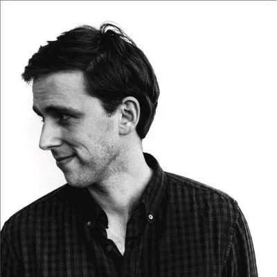 Black and white portrait of a man in a checkered shirt looking to the side.