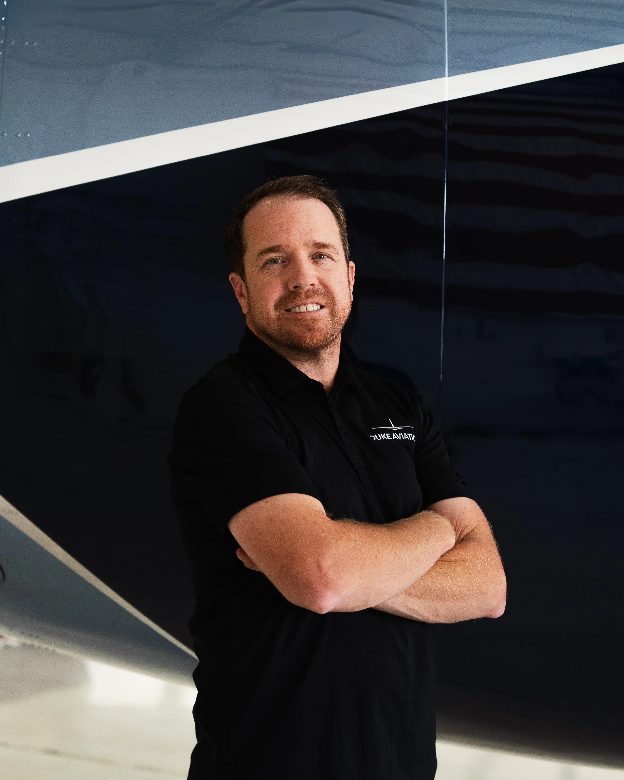 Person wearing a "Duke Aviation" polo shirt standing in front of an aircraft.