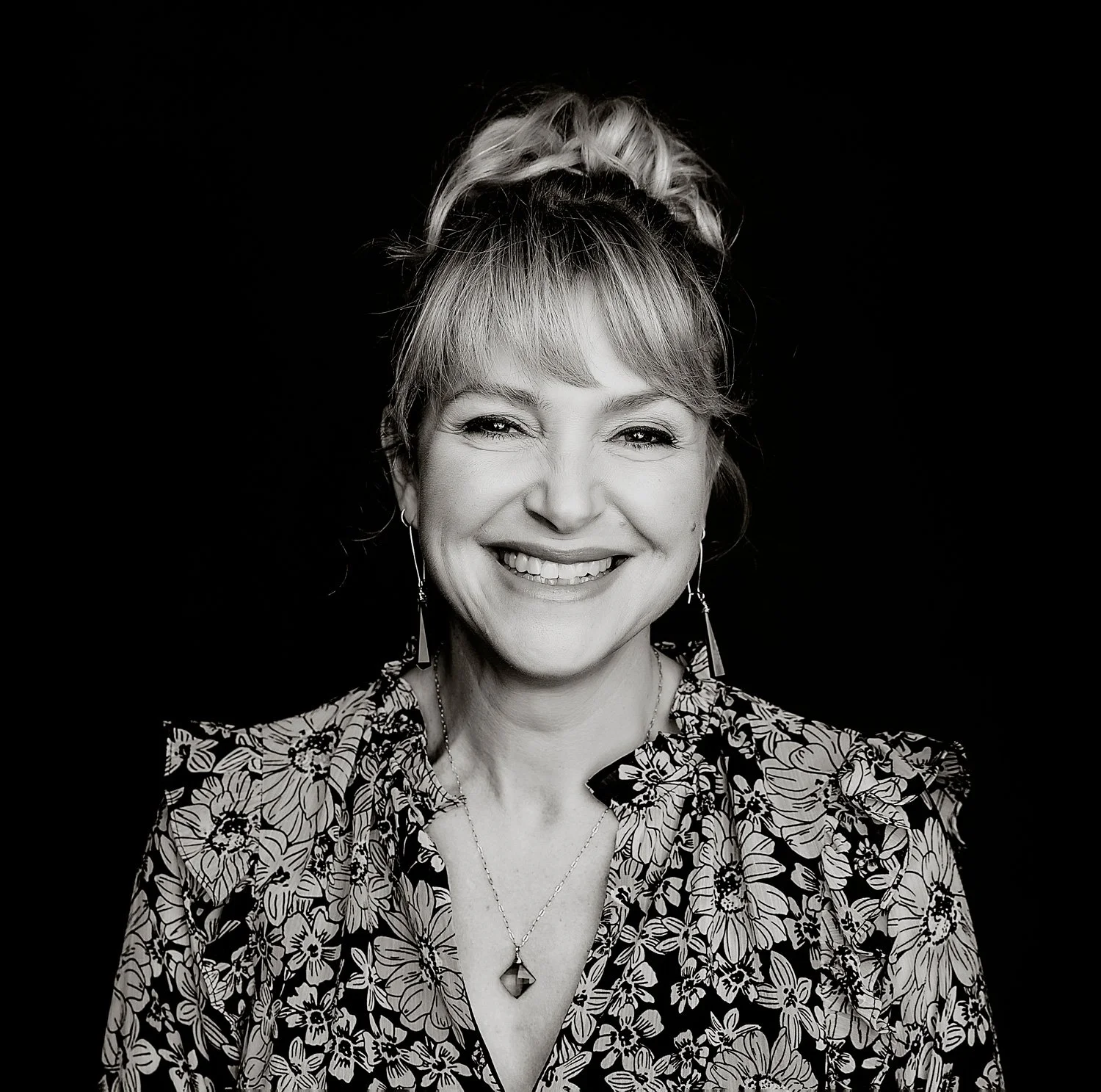Laura Beauparlant in a floral blouse with a necklace, black background.