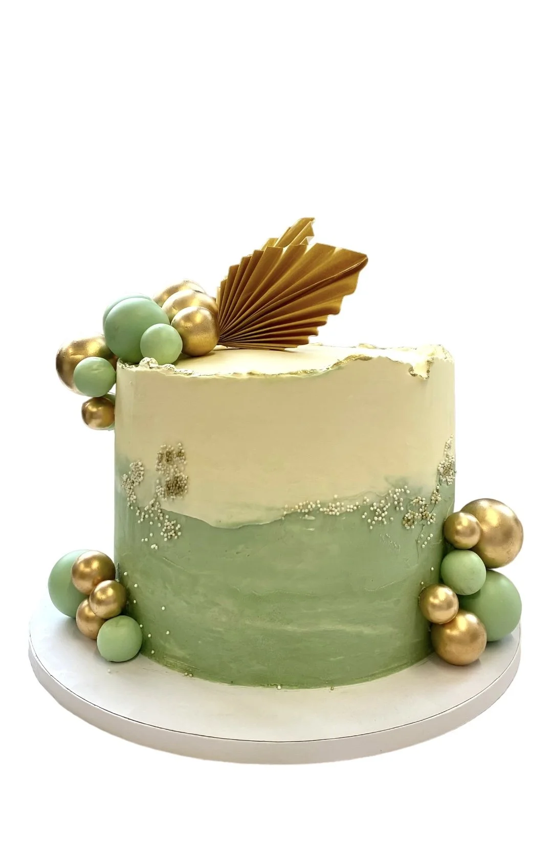 Elegant cake with green and cream icing, gold and mint decorative spheres, gold fan topper, and white sprinkles.
