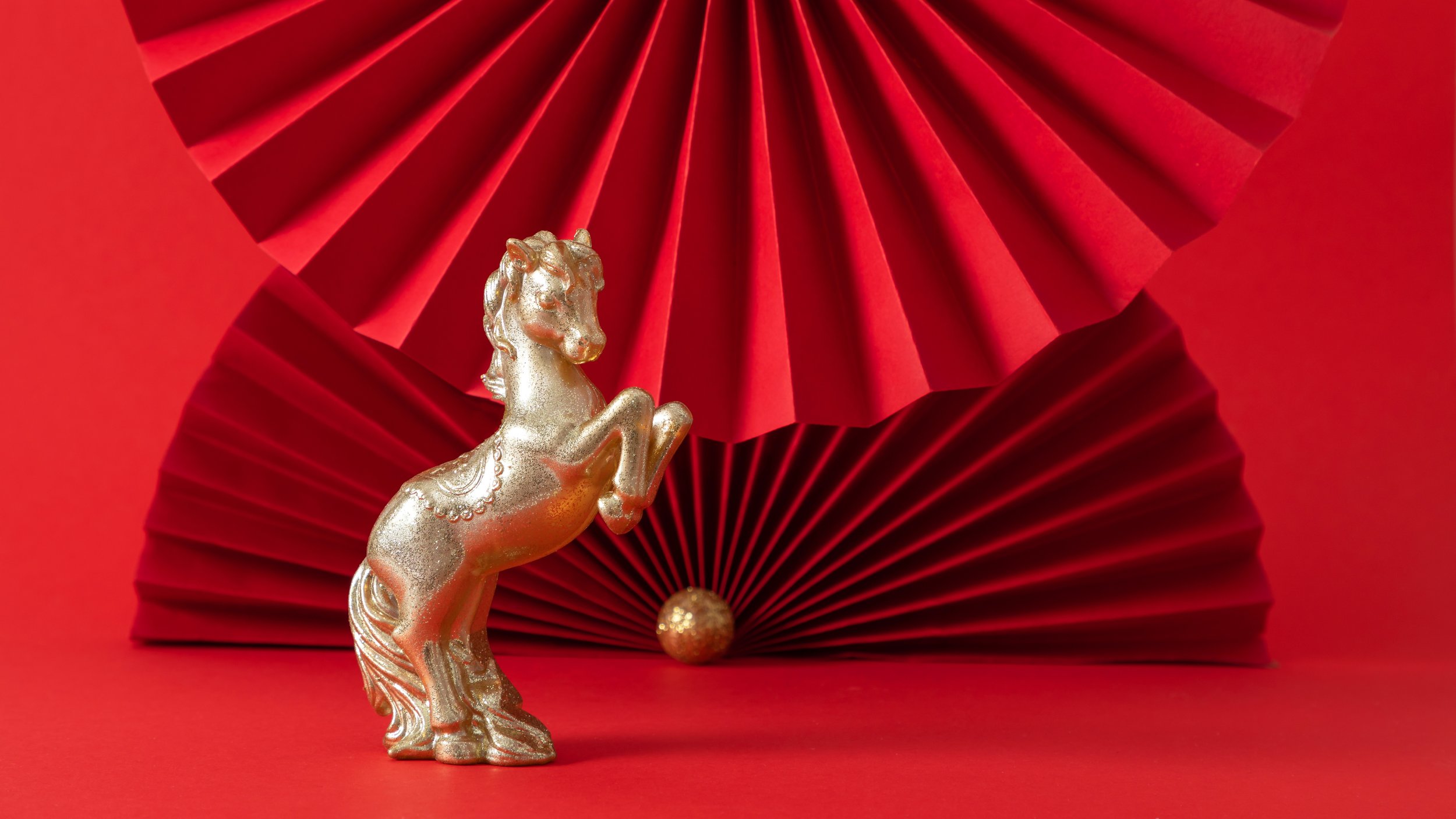 A golden horse figurine stands on hind legs in front of 2 red paper fans