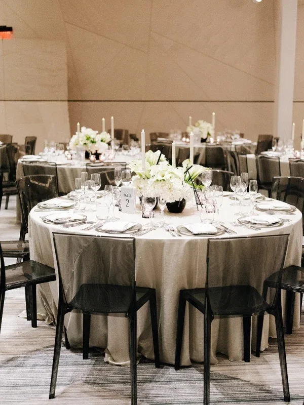 Wedding reception table decorated with white flowers, candles, and glassware in a banquet hall.