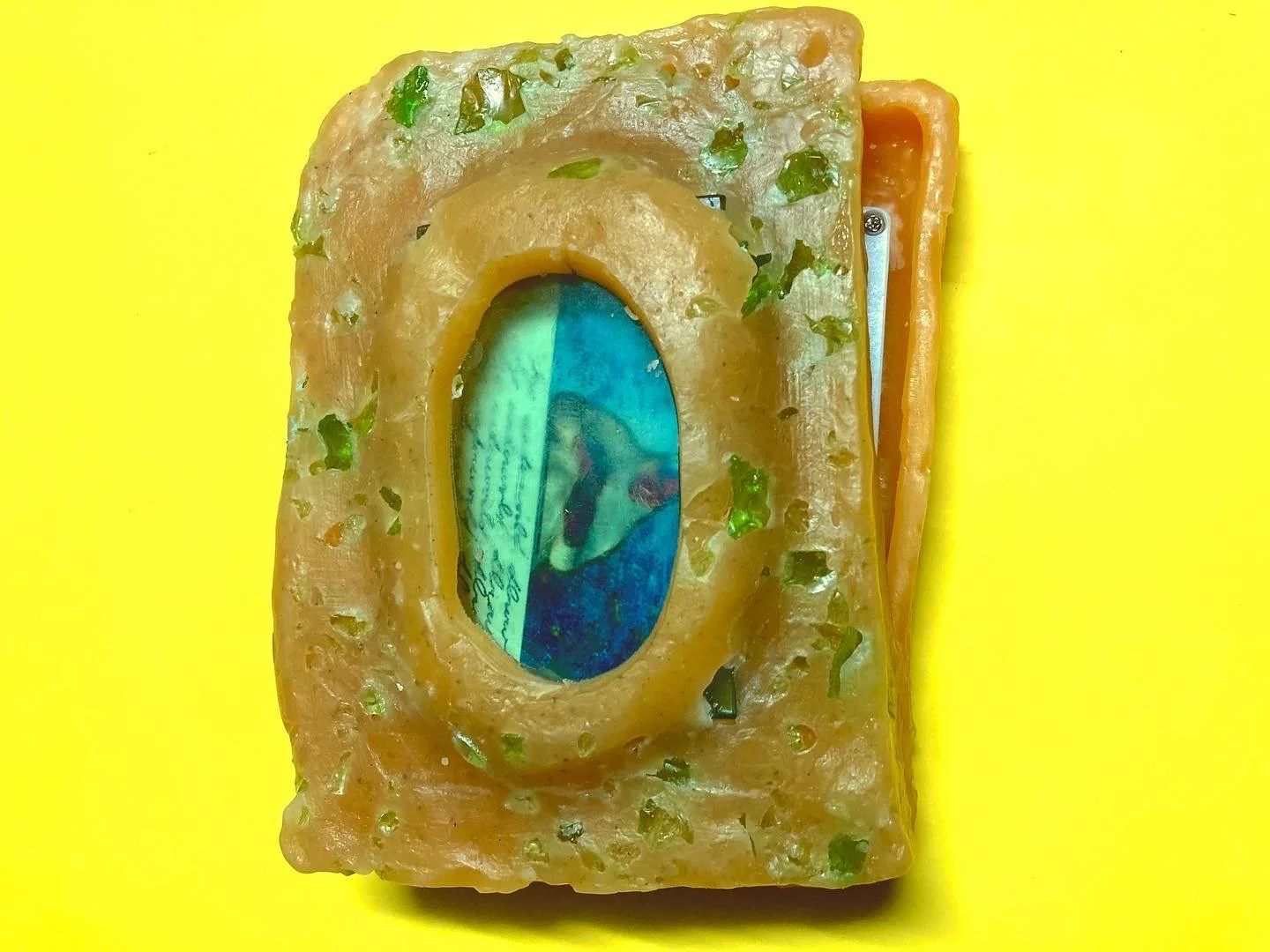 A wax case with cassette print featuring text and a blue-ish figure embedded inside, resting on a yellow background.