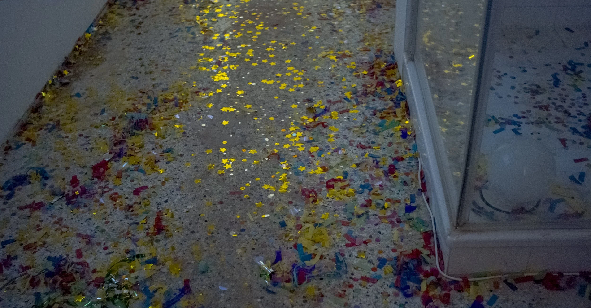 Colorful confetti scattered on a speckled floor near a glass door reflection.