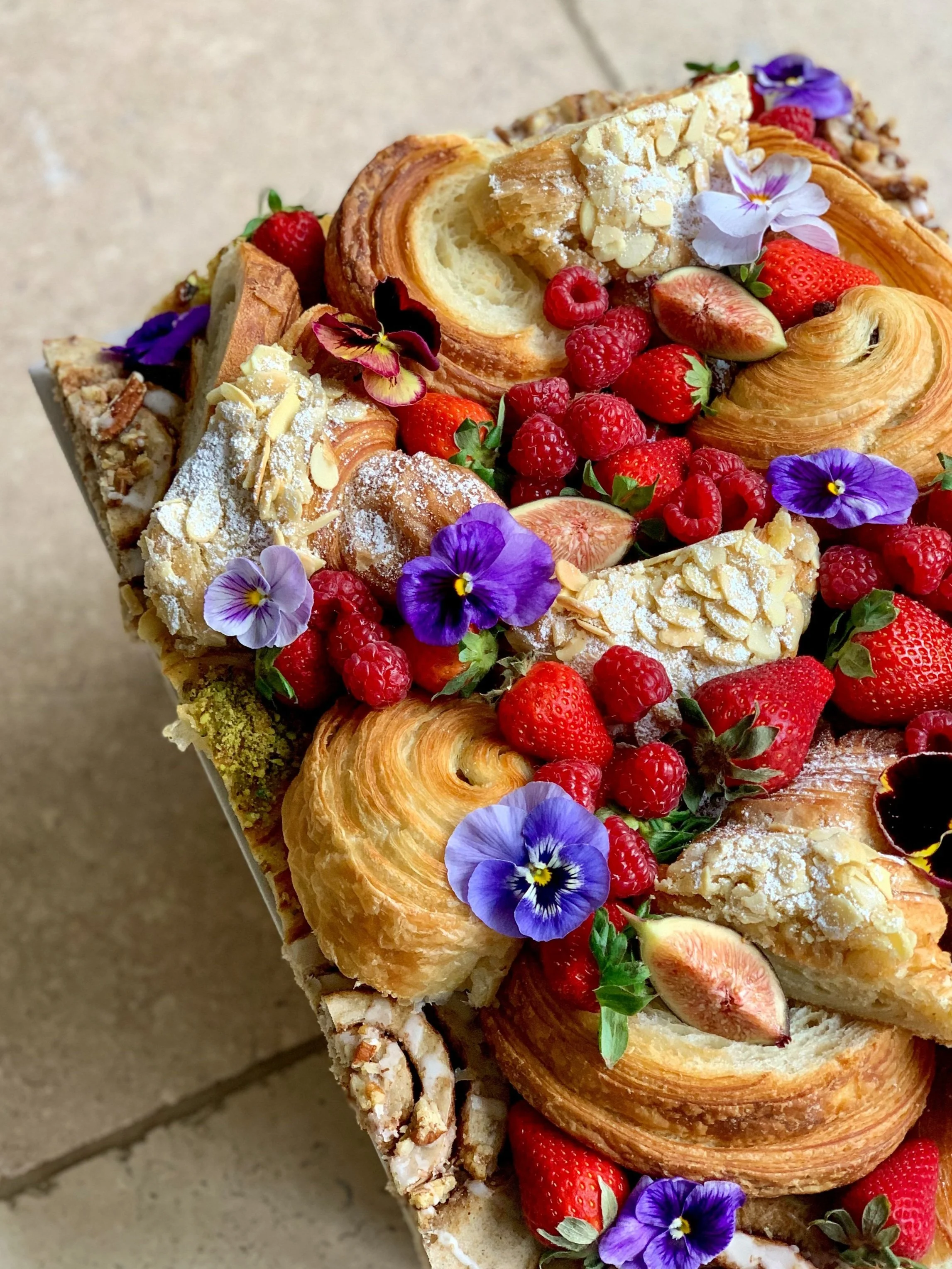 Close-up of a decorated pastry platter with various puff pastries, strawberries, raspberries, sliced figs, edible flowers, and almonds.
