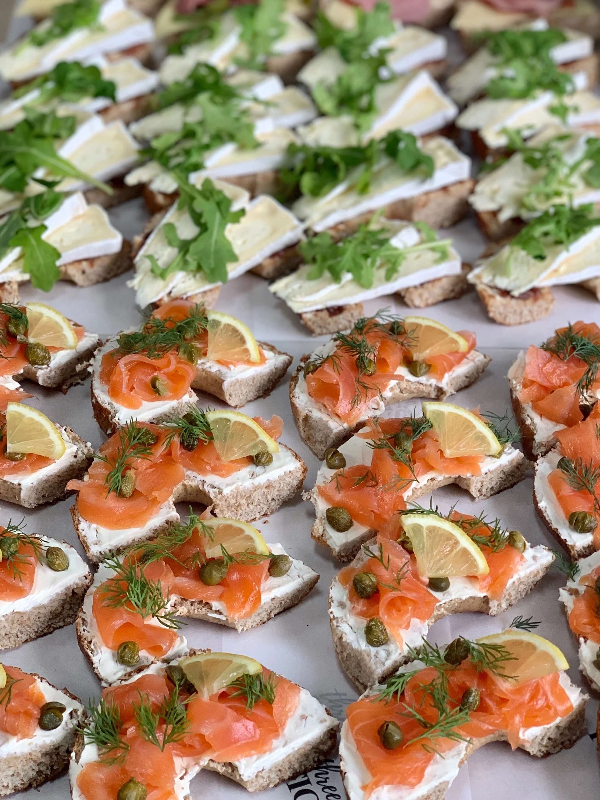Assorted open-faced sandwiches with various toppings including smoked salmon, avocado, meats, cheese, lemon slices, capers, and herbs on different types of bread.