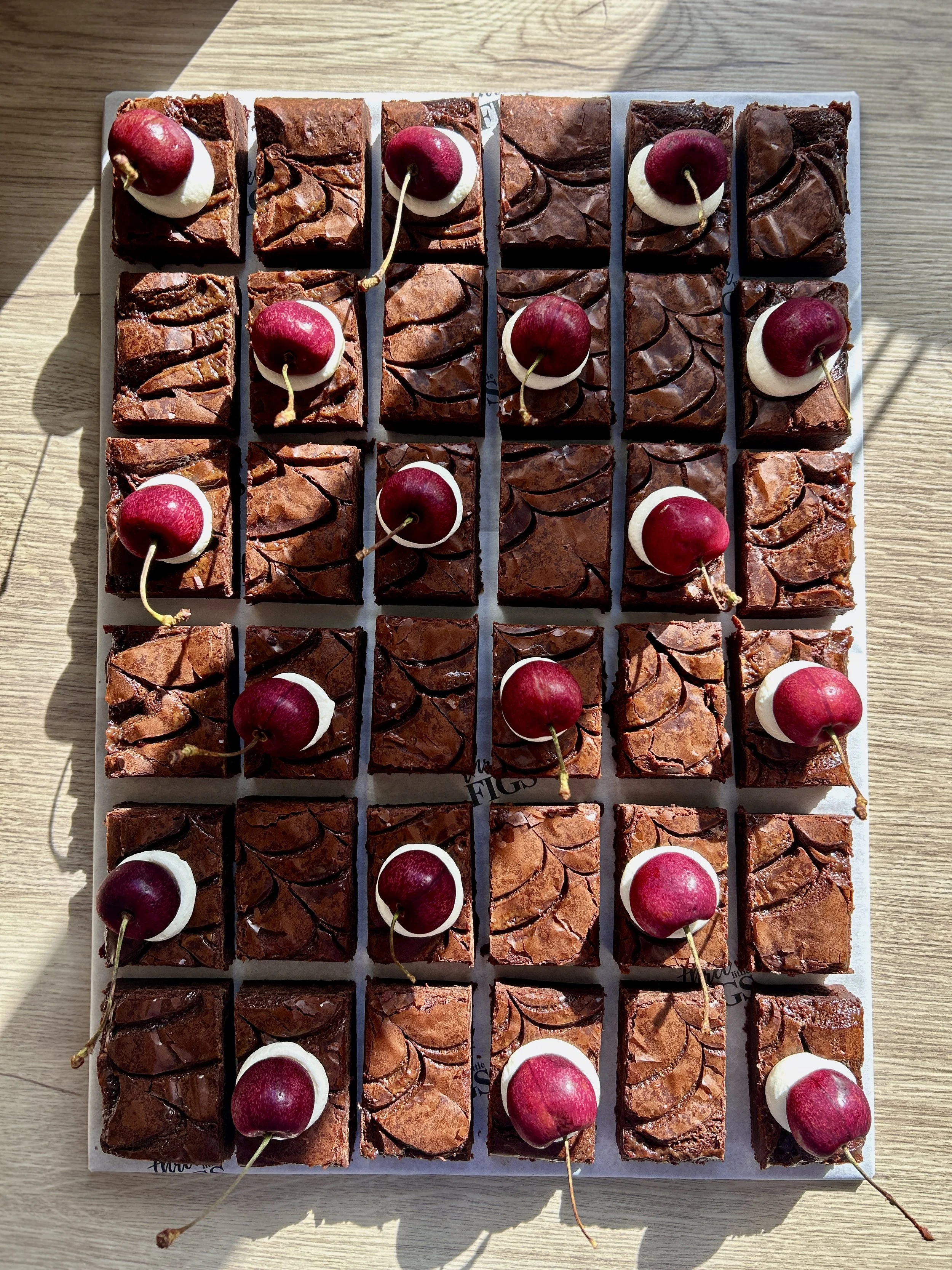 Chocolate brownies topped with raspberries and mint leaves on a white tray.