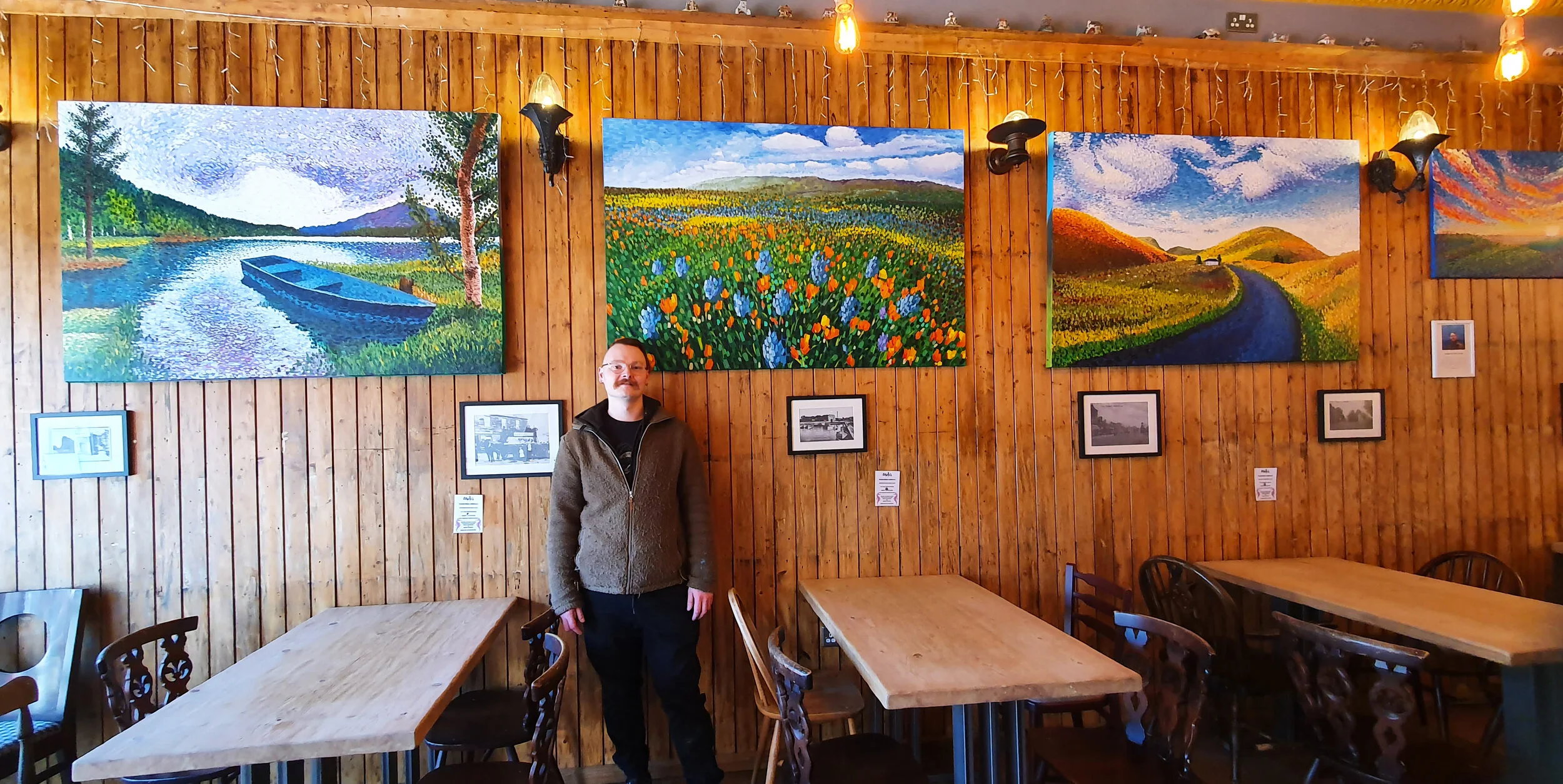 Artist standing in front of paintings in an exhibition of pointillist artwork