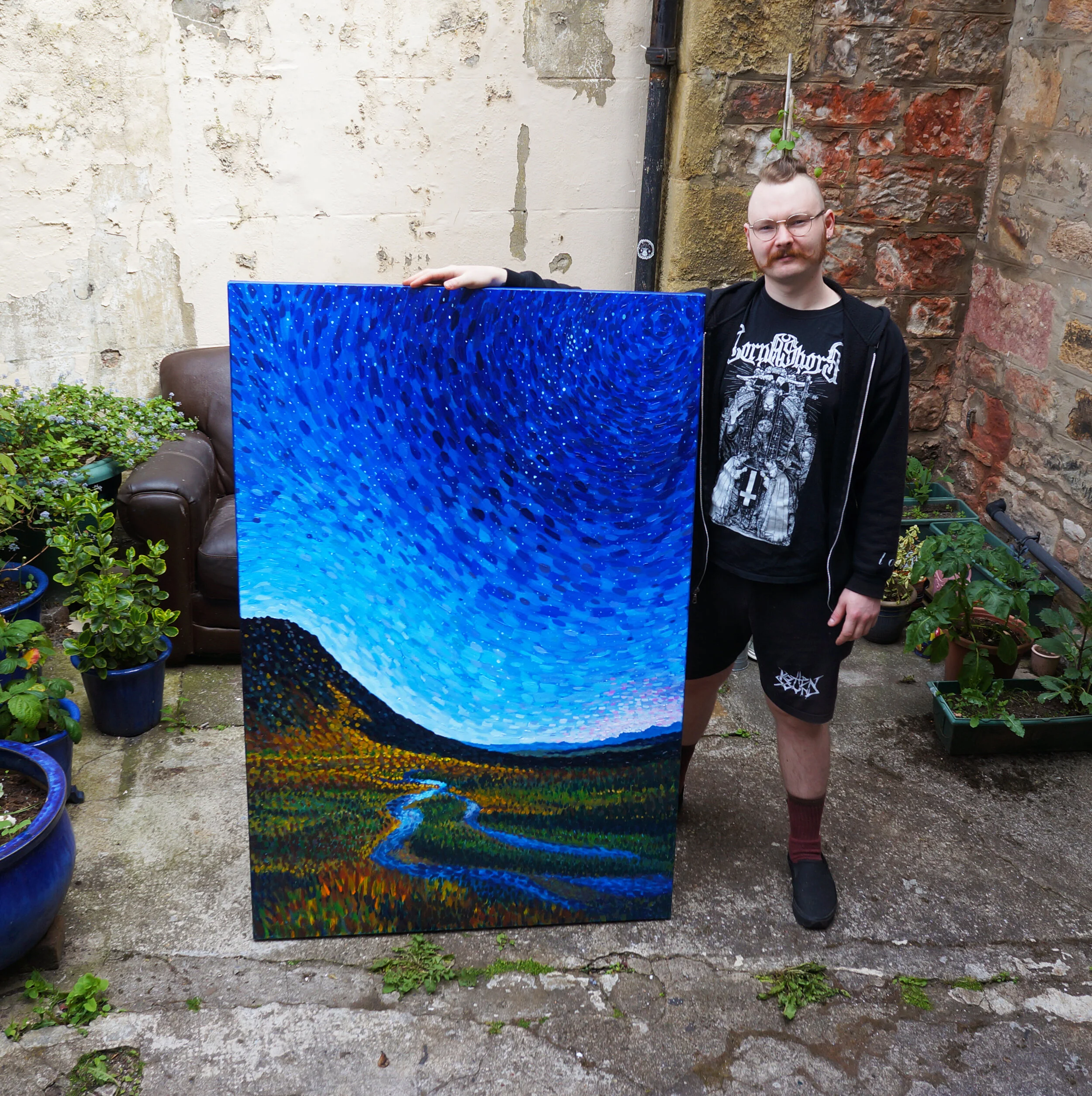 Artist standing with a beautiful blue painting of a night sky