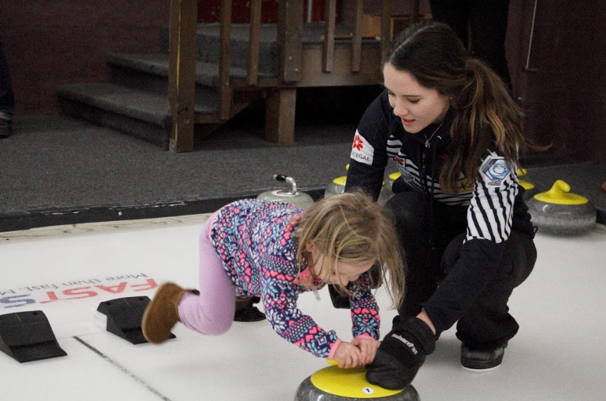  Jenna Burchesky instructs a tiny aspiring-curler, brought in by Korey Dropkin's presentations at schools. 