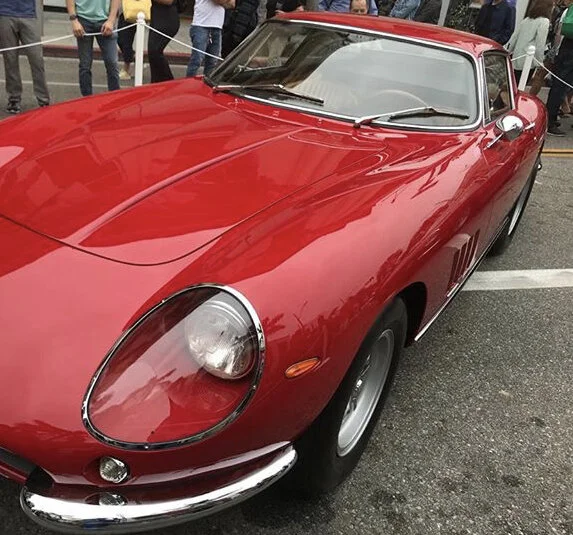 A classic red sports car displayed at an outdoor event with people in the background.
