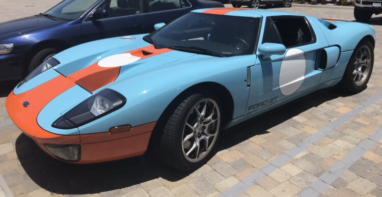 A Ford GT sports car with a racing livery in blue, orange, and white parked on a brick-paved area.