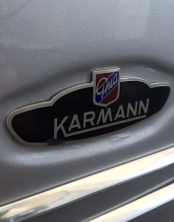 Close-up of a Karmann Ghia emblem with the Karmann logo on a vehicle, likely the front grill.