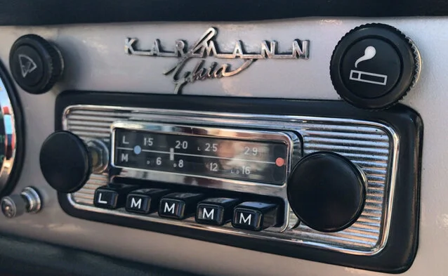 Close-up of a vintage Klarmann radio dashboard with an analog tuning dial, switches labeled L and M, and a circular knob for volume or tuning, in a classic car interior.