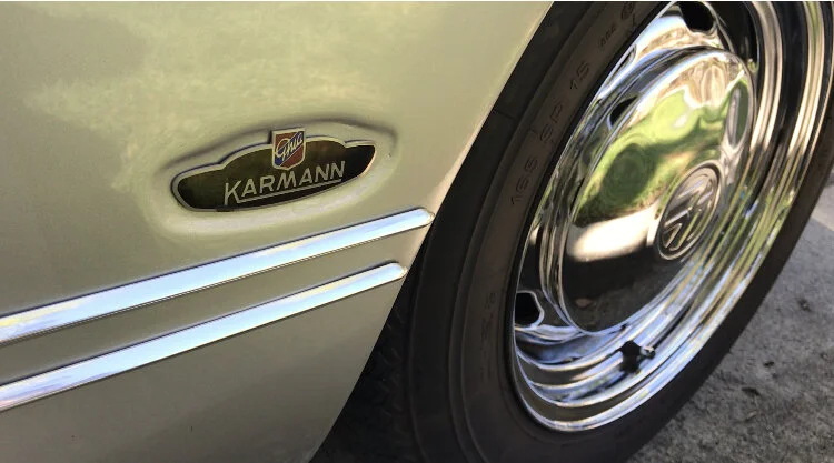 Close-up of a vintage Karmann Ghia car displaying the Karmann badge and chrome wheel.