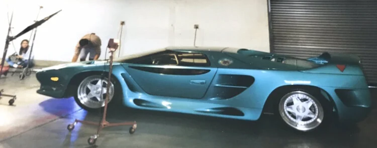 Blue sports car on a photo shoot set with crew and equipment around it.