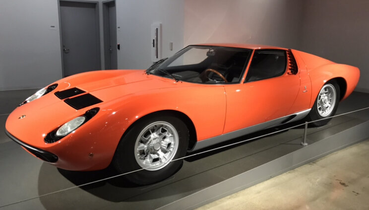 An orange Lamborghini Miura on display in a museum.