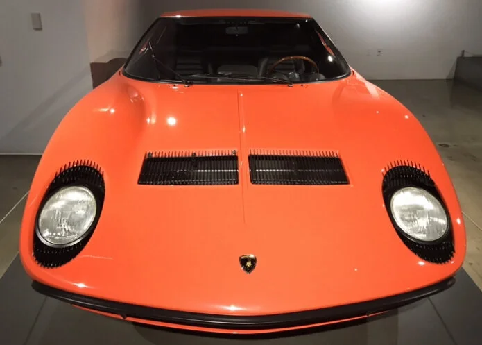 Orange vintage Lamborghini Miura with black vents on the hood and round headlights.