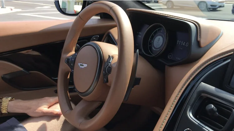Inside view of a luxury car with a tan leather steering wheel and dashboard, showing a digital display and control buttons.