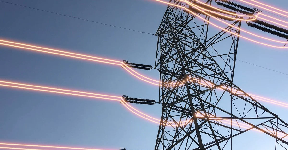 Close-up of an electric power transmission tower with glowing power lines against a blue sky.