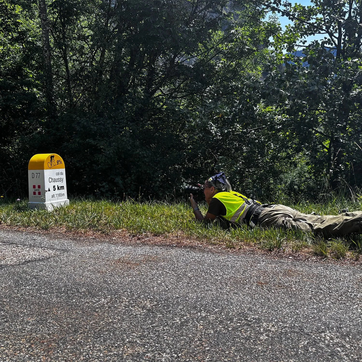 Karen Yeomans lying at the roadside beside the Col du Chaussy marker to photograph a mountain stage climb