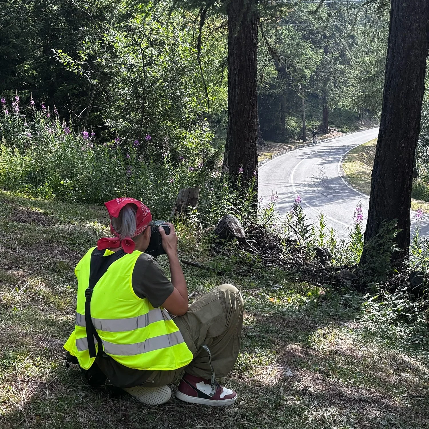 Photographer in a high visibility vest kneeling at the roadside with a camera on an alpine bend