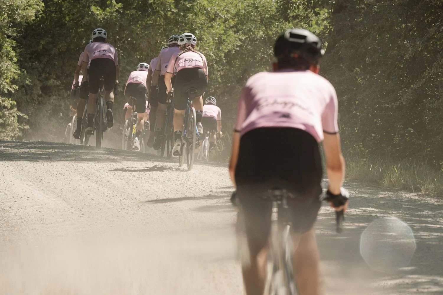 Rider in a pink jersey from behind on a dusty gravel road with a group ahead in the dust