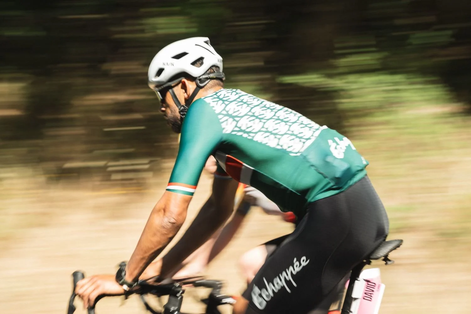 Panning shot of a cyclist in a green Échappée jersey against a blurred golden background