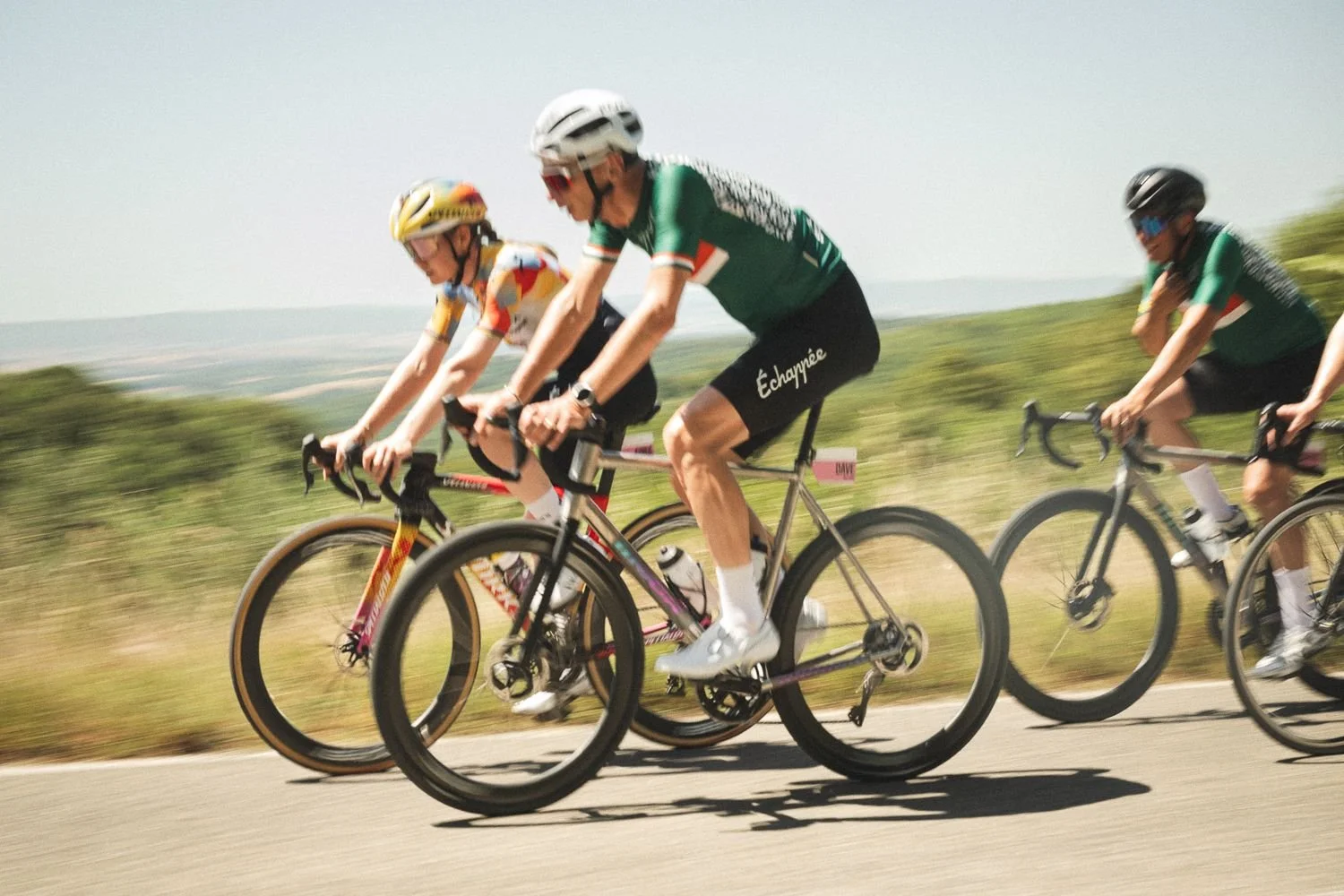 Three cyclists riding fast on a Tuscan road in a panning shot with the hills blurred behind