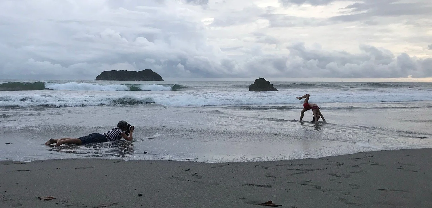 Karen Yeomans lying on wet sand to photograph a yoga practitioner at the shoreline for a retreat brand