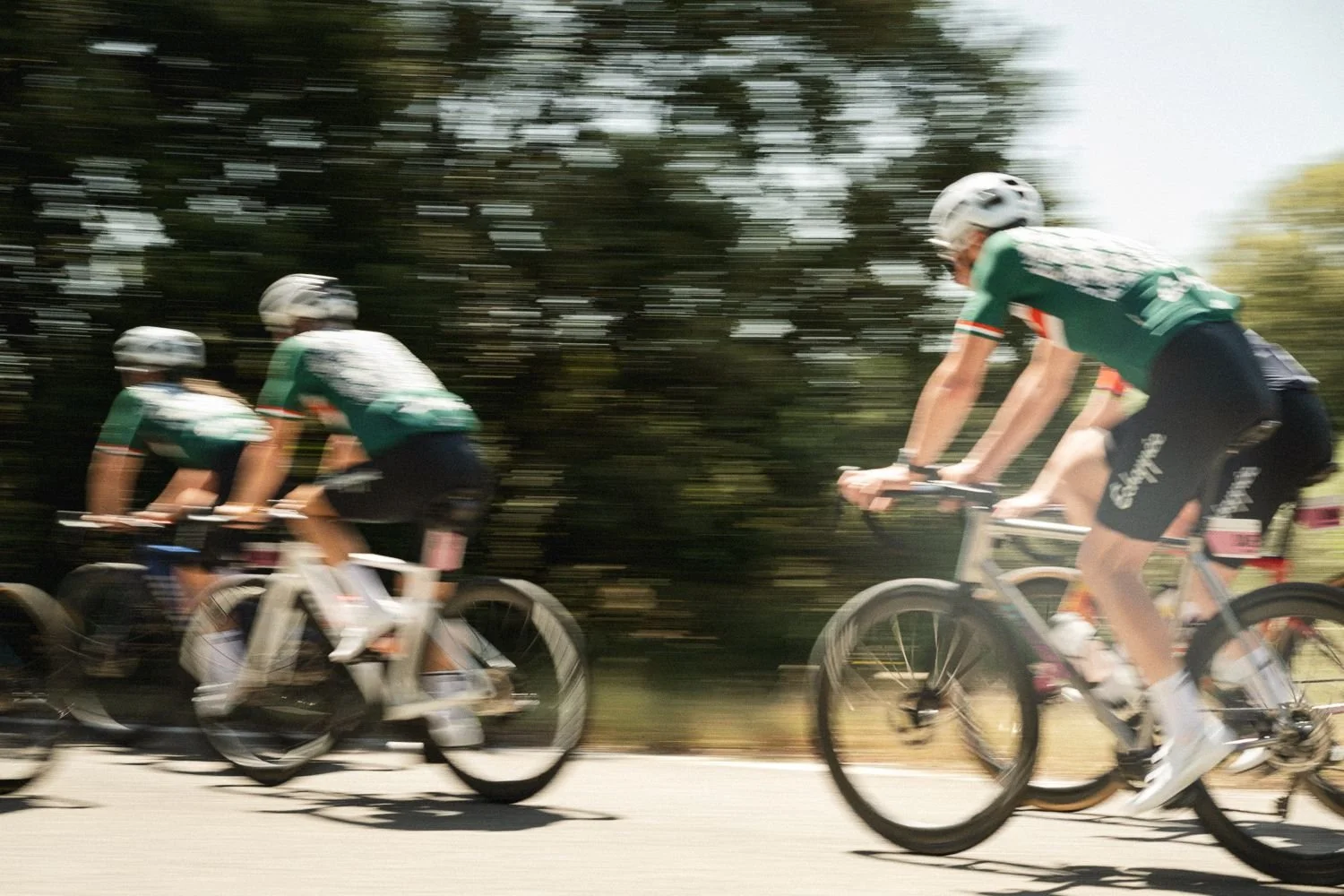 Panning shot of three cyclists in green jerseys with blurred trees behind