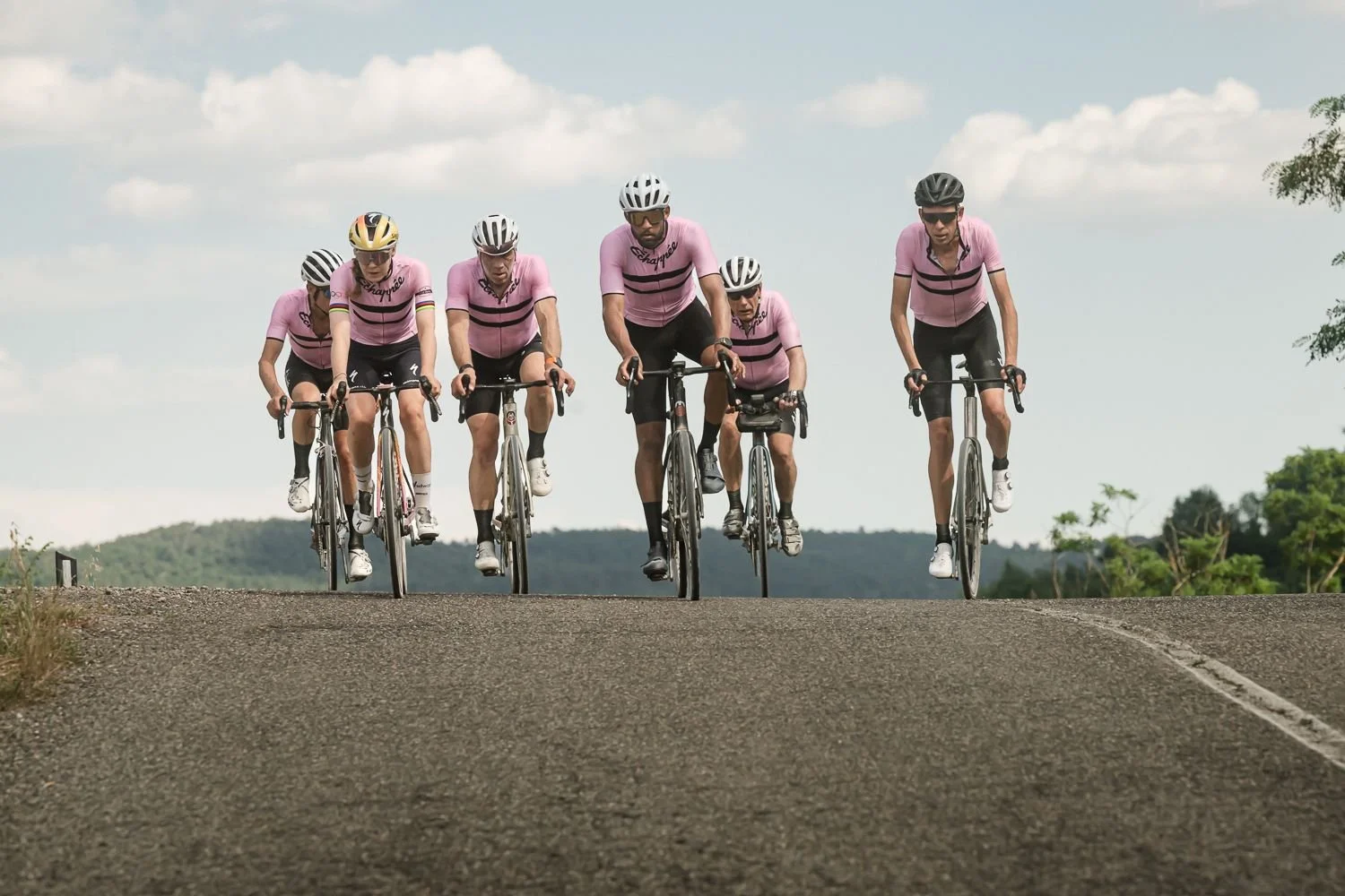 Six cyclists in pink jerseys riding towards the camera along an empty road