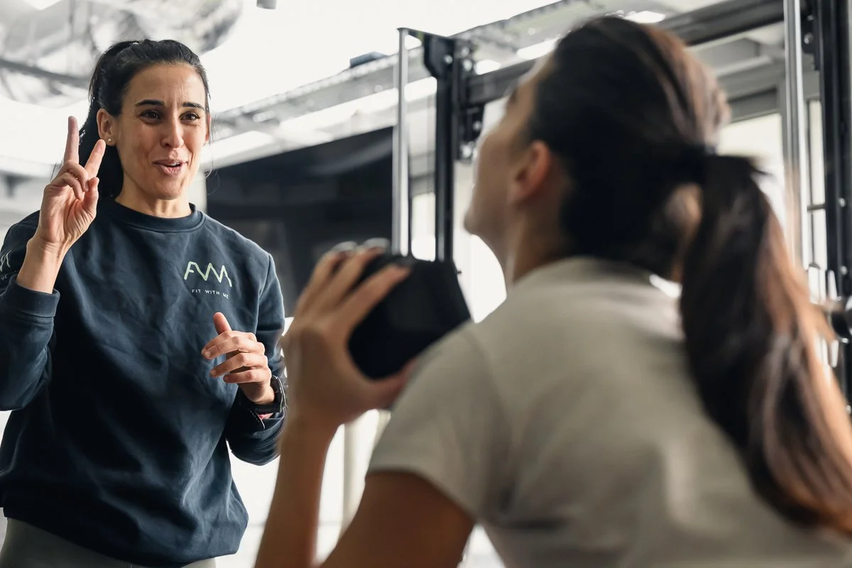 Fit With Me trainer holding up two fingers as she explains an exercise to a client holding a dumbbell