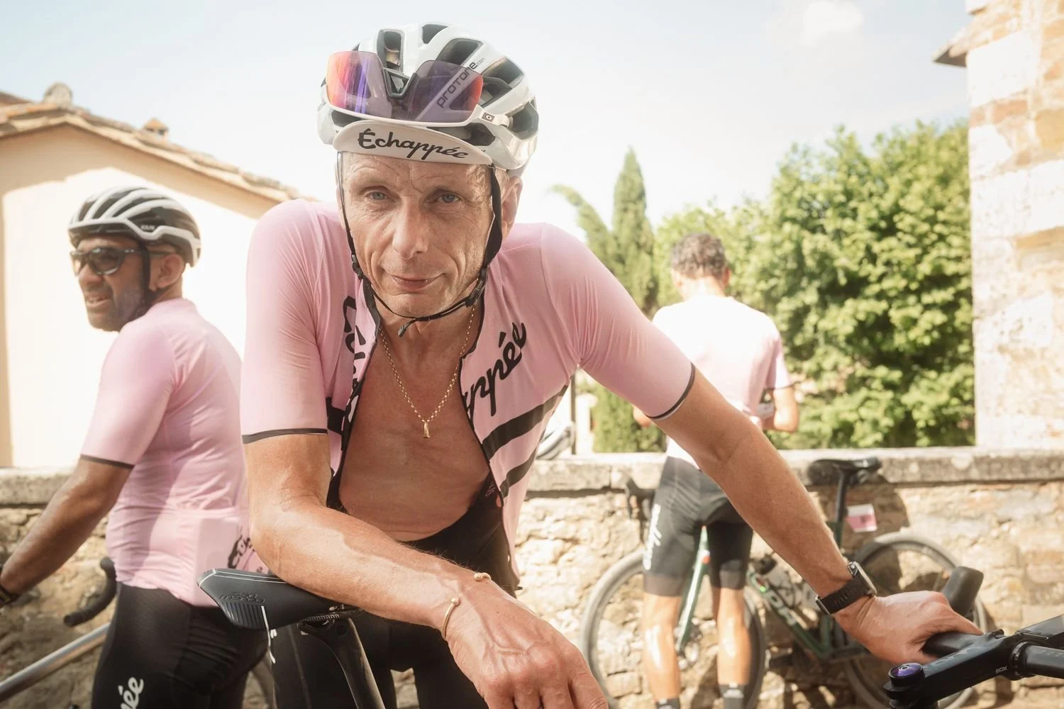 Portrait of a cyclist in a pink Échappée jersey and helmet at a stone walled rest stop