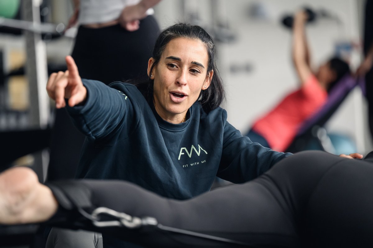 Trainer in a Fit With Me sweatshirt pointing out a correction to a client mid exercise