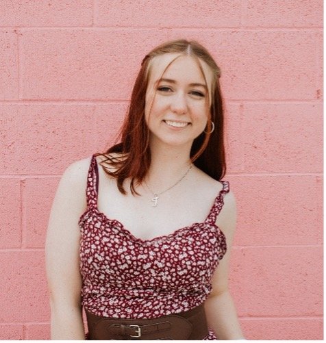 Jacey, smiling, wearing a red and white top in front of a pink brick background